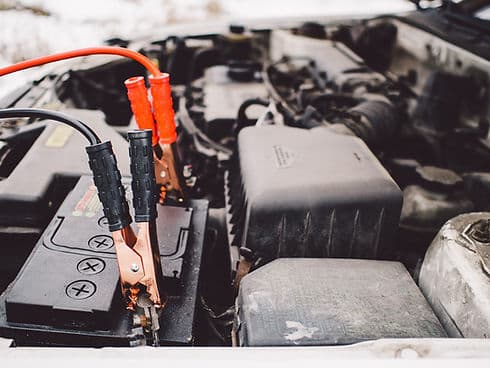 Jumper clamps on a car battery under the hood, outdoors.